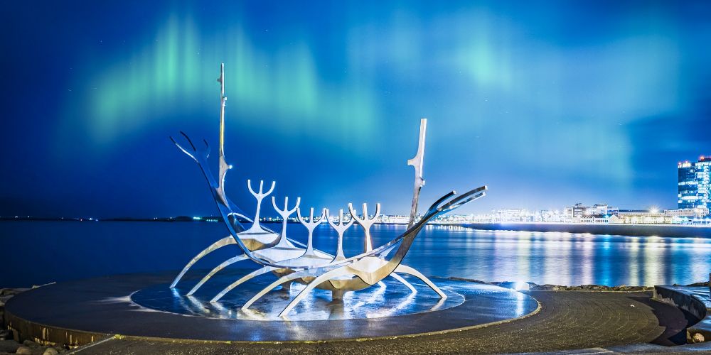 view of Reykjavik city at night with Sun Voyager sculpture and Northern Lights