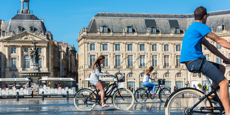 people-riding-bicycles-in-the-mirror-fountain-in-front-of-place-de-la-bourse-in-bordeaux-france