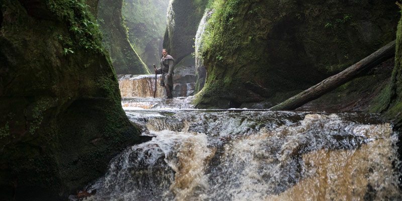 Charlie Hunnam as King Arthur standing on a rock in the river at the Devils Pulpit Finnich Glen, Killearn, Scotland