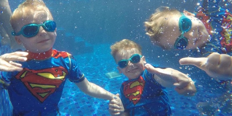 three boys in Superman rash vests give a thumbs up under the water in a pool at Al Wadi Resort