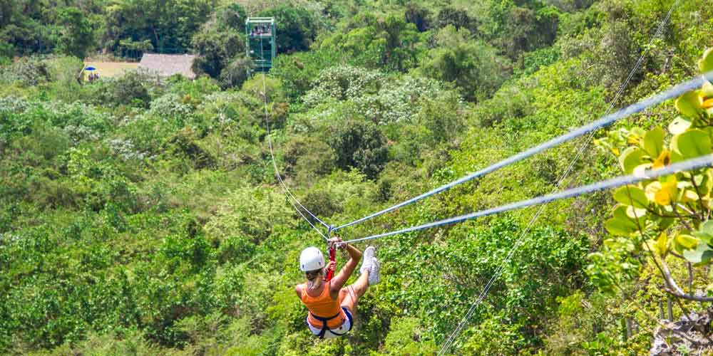 woman in safety gear on zipline high above treetop canopy 