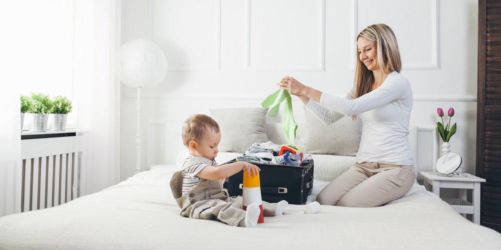 mother packing suitcase with baby - tips for your first holiday with a baby