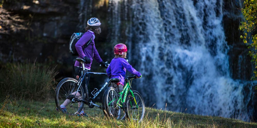 cyclists in front of waterfall - things to do in June