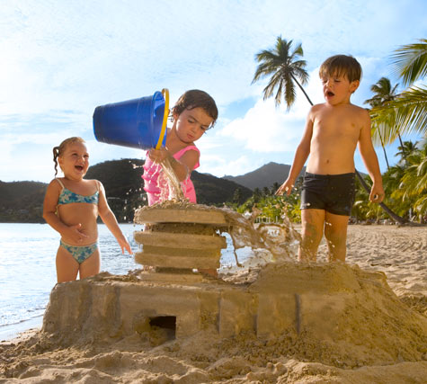 Children on the beach with a sandcastle. One child is pouring a bucket of water over the sandcastle.