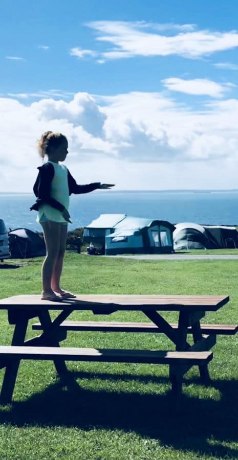 Best family coastal campsites, girl stands on table at campsite by sea