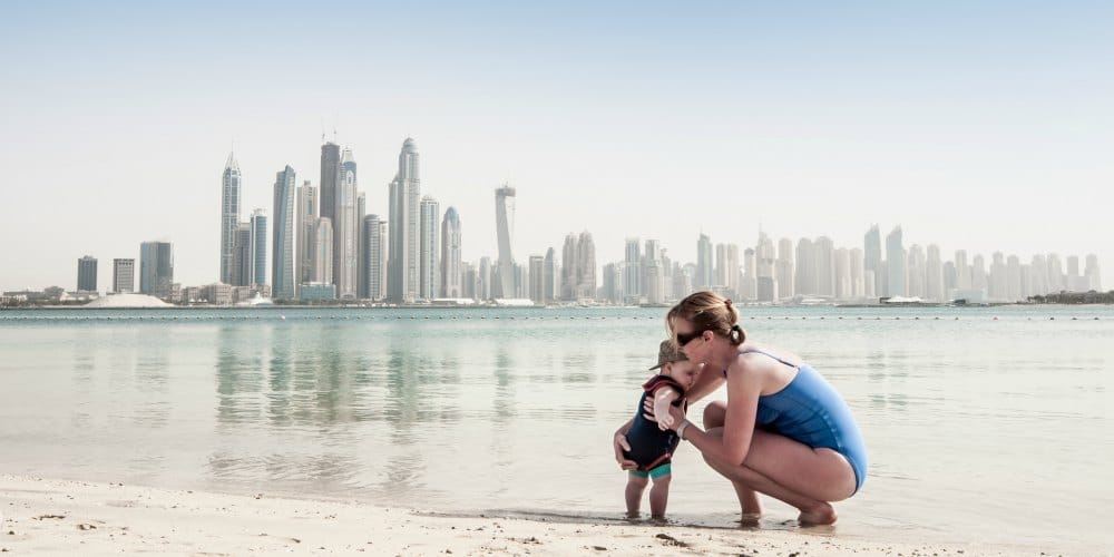 best family holiday destinations 2019, mother and son on beach Dubai, skyscrapers background