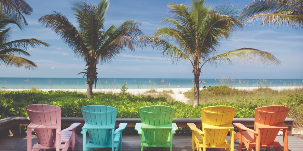 florida-family-holidays-anna-maria-island-colourful-adirondak-chairs-facing-palm-tree-lined-gulf-coast-beach