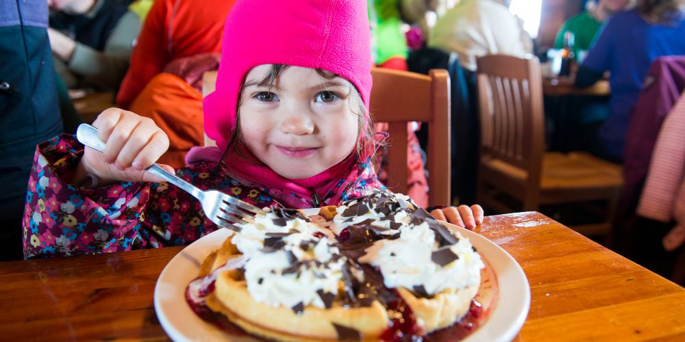 little-girl-wearing-ski-hat-eating-pancakes-and-cream-family-ski-day-lunch-whistler-resort-canada