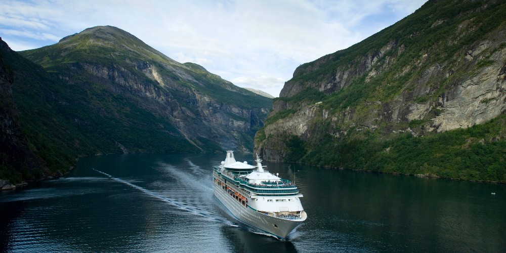 geiranger-royal-caribbean-ship-at-sea-surrounded-by-mountains-in-Norwegian-fjords-under-a-blue sky