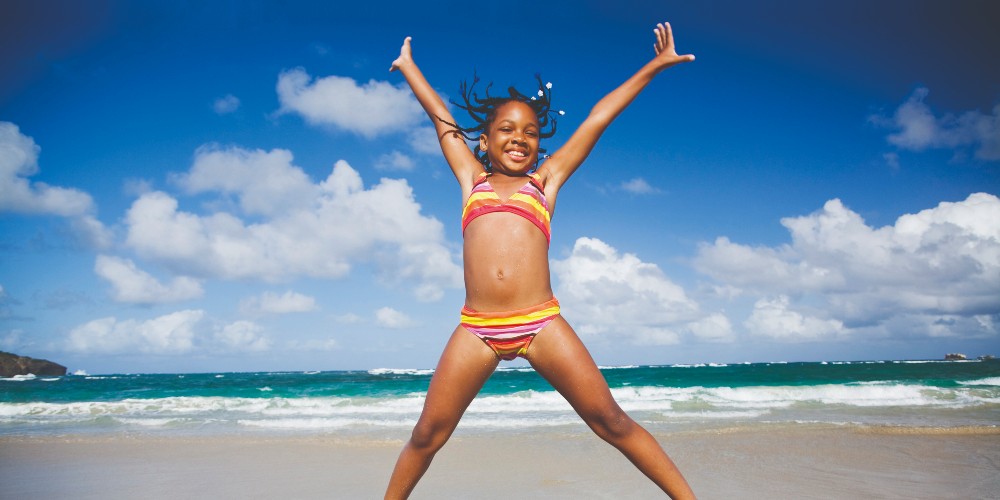 caribbean-island-holidays-young-girl-doing-star-jumps-in-stripey-bikini-on-caribbean-beach