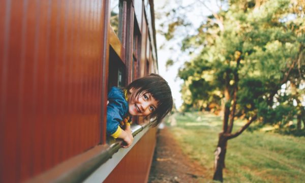 family-rail-holidays-laughing-child-looking-out-of-vintage-train-travelling-through-countryside