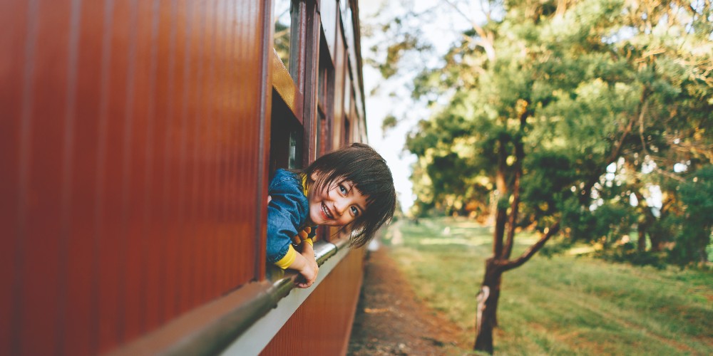 family-rail-holidays-laughing-child-looking-out-of-vintage-train-travelling-through-countryside