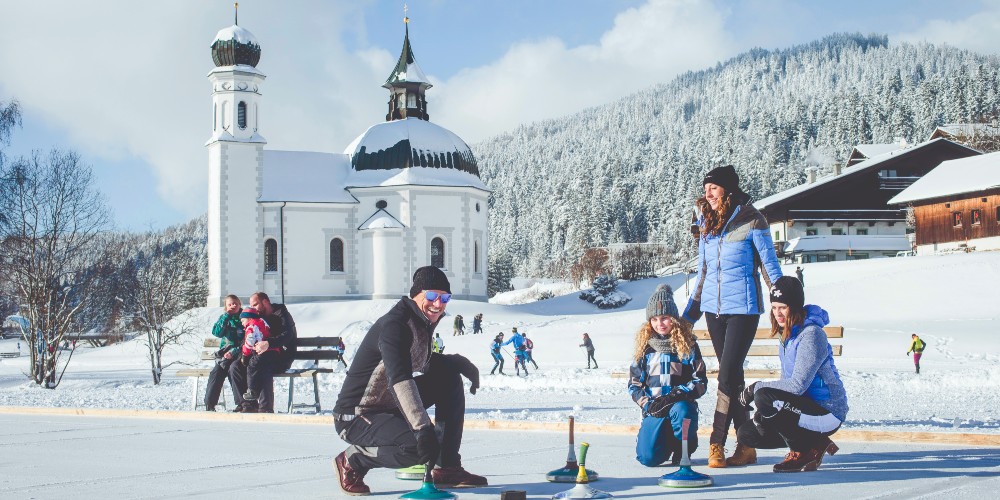 seedel-austria-family-curling-in-village-centre-with-onion-domed-church-in-background-winter-2022