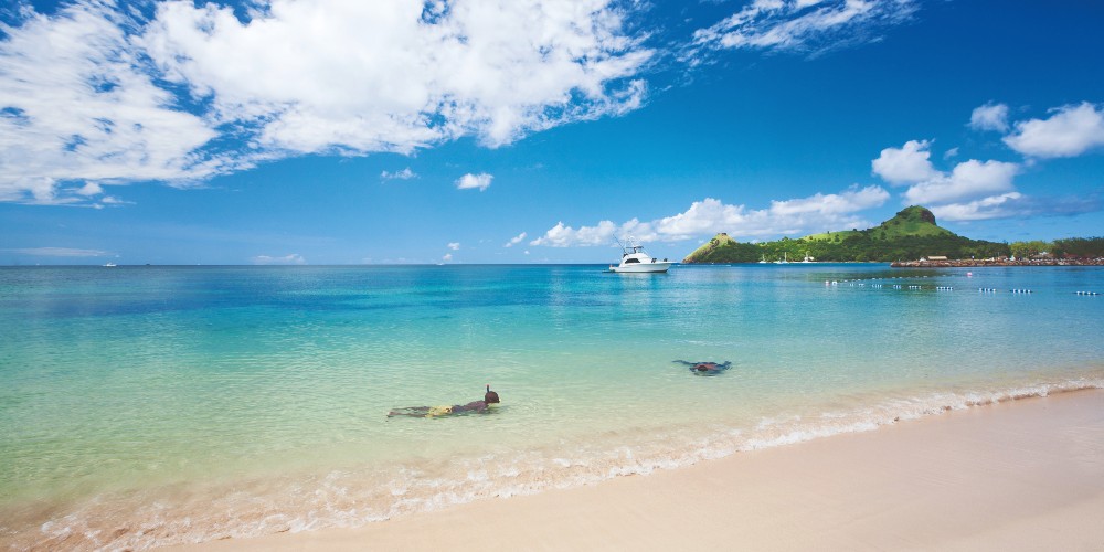 men-snorkeling-in-shallow-caribbean-seas-white-sand-beach-island-yeachts-blue-skies-family-traveller