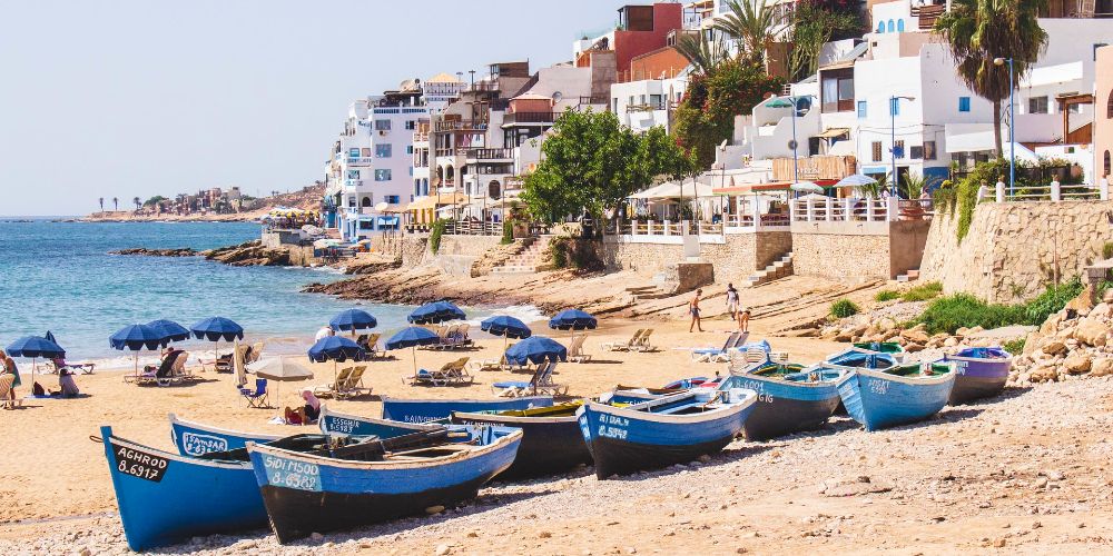 taghazout-morocco-blue-boats-on-a-sunny-beach-with-white-houses-and-blue-sun-umbrellas-louis-hansel
