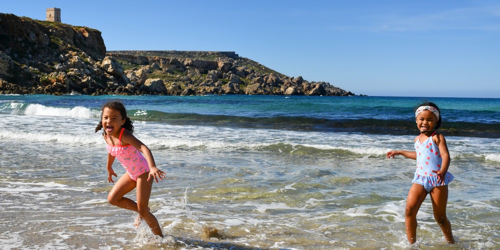 two-young-girls-in-swimsuits-splashing-in-the-sea-at-golden-bay-beach-family-holidays-in-malta-2022