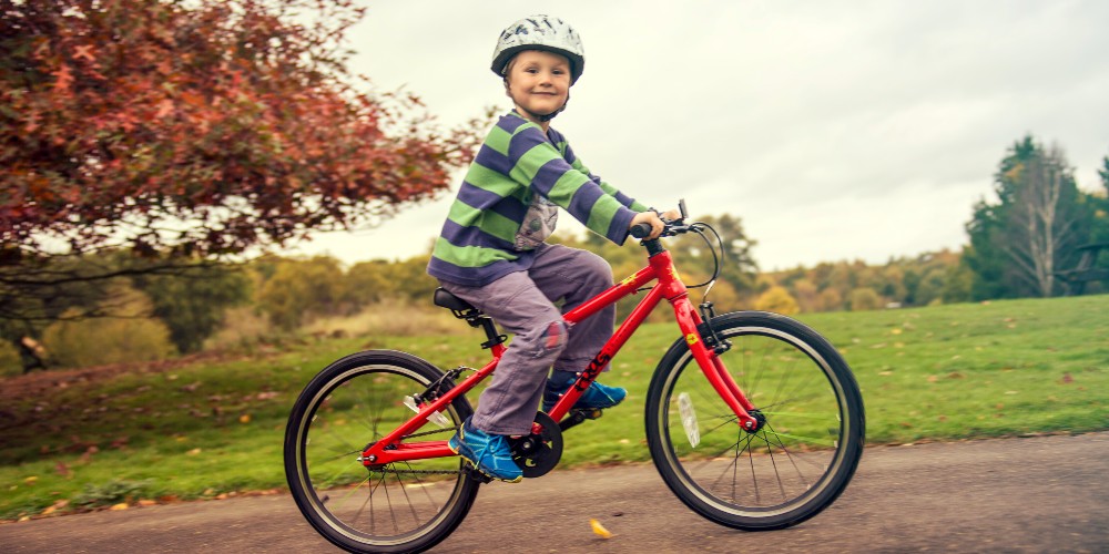 young-boy-wearing-cycling-helmet-riding-red-bicycle-through-leafy-park-family-traveller-2022