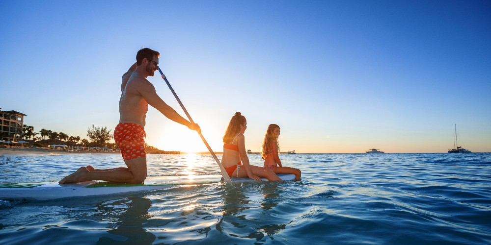 family-paddleboarding-sunset-blue-seas-beach