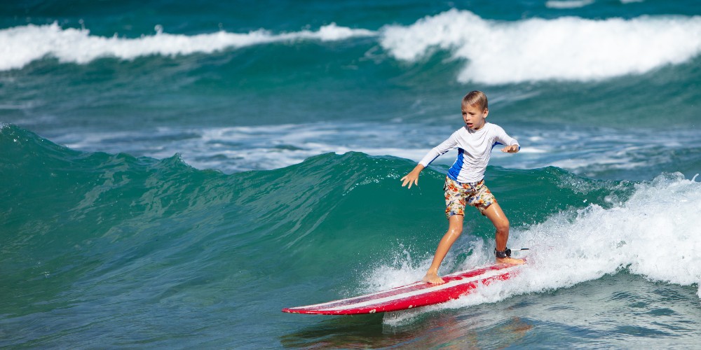 young-boy-surfing-lessons-board-shorts-rash-vest