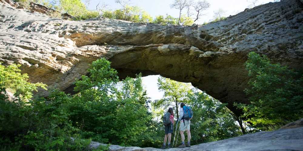 two-hikers-standing-under-natural-bridge-with-rucksacks-during-summer