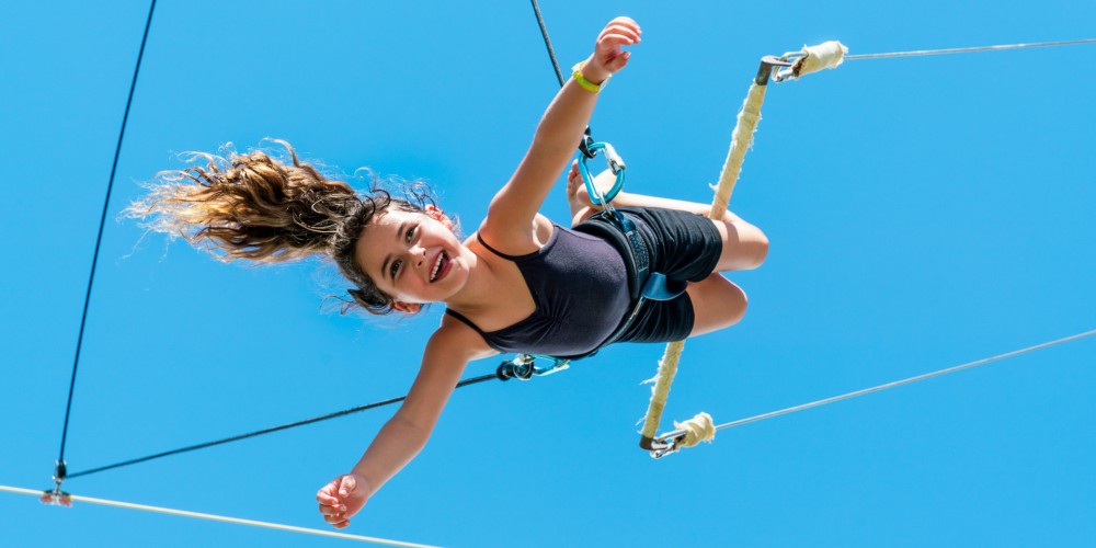 Circus School by Club Med laughing young girl in safety harness on trapeze