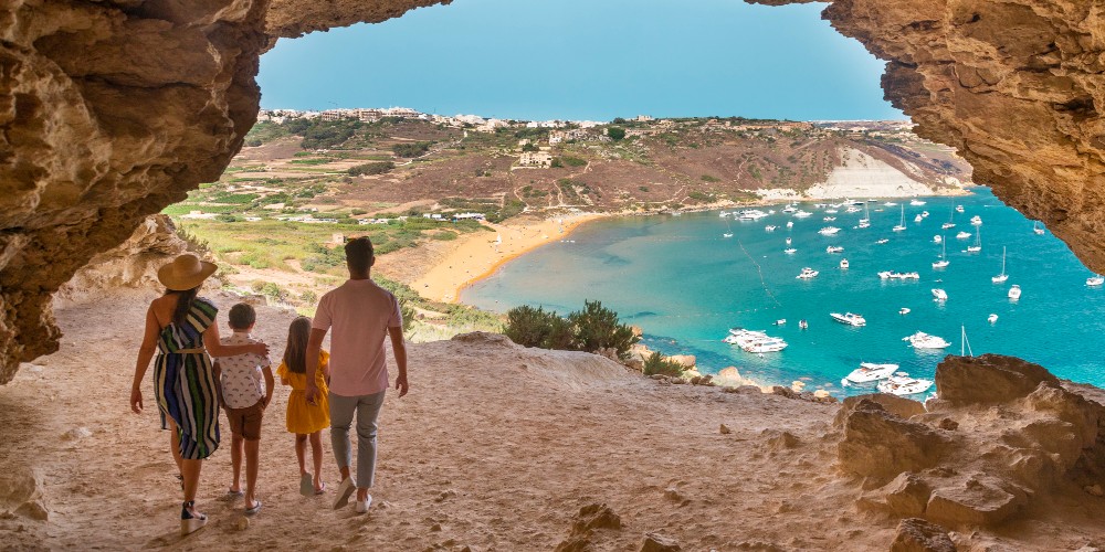 family-standing-under-natural-stone-arch-overlooking-ramla-bay-mediterranean-beach-2022