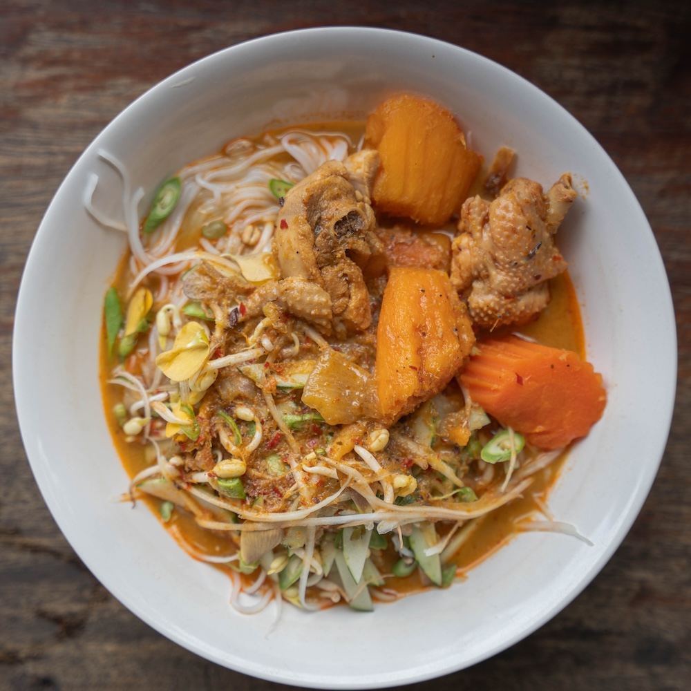 Bowl of white noodles with carrot, chicken and an orange gravy
