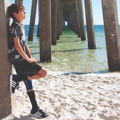 boy-in-long-shorts-black-and-white-soccer-shirt-standing-under-pilings-pensacola-pier-2022